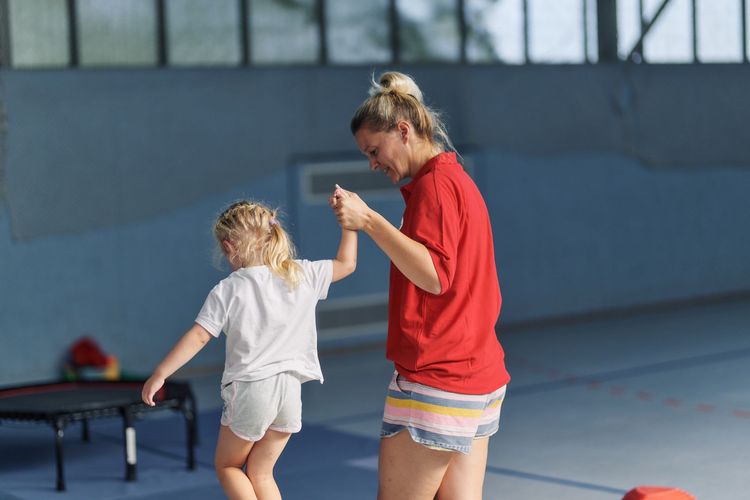 Trainerin unterstützt Kleinkind beim Kinderturnen.