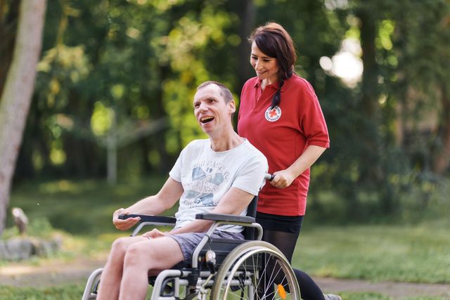 Eine Mitarbeiterin schiebt einen Nutzer im Rollstuhl durch den Park
