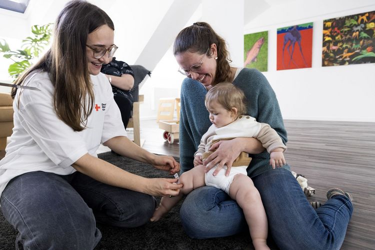 Mutter mit ihrem Baby und Mitarbeiterin vom DRK. Das Kind erhält ein Heftpflaster auf das Knie
