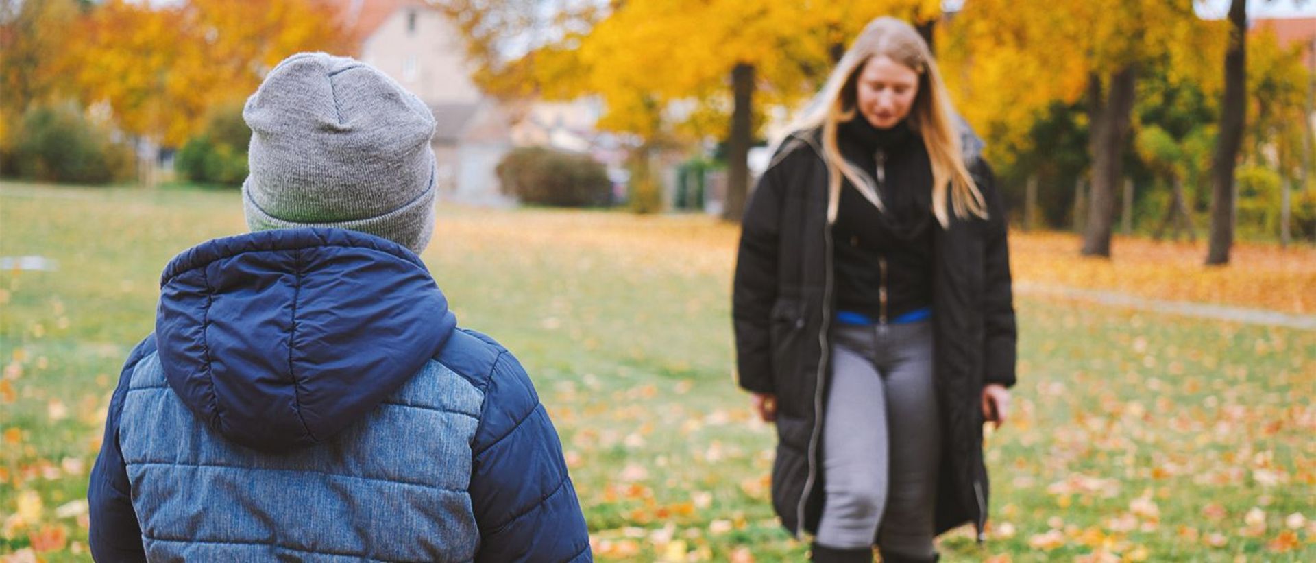 Auf dem Bild sieht man einen Jungen, der mit einer erwachsenen Dame im Park Fußball spielt.