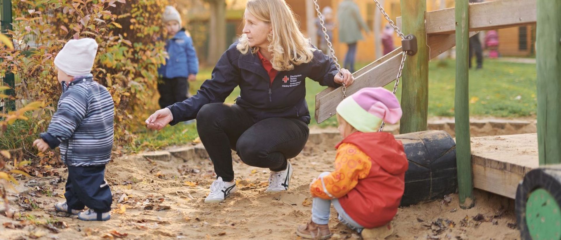 Erzieherin spielt mit Kindern im Sandkasten.