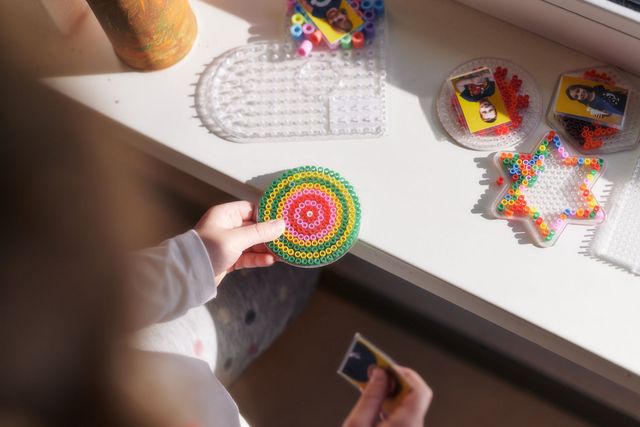 Kinderhände bereiten ein Bild aus Bügelperlen vor.