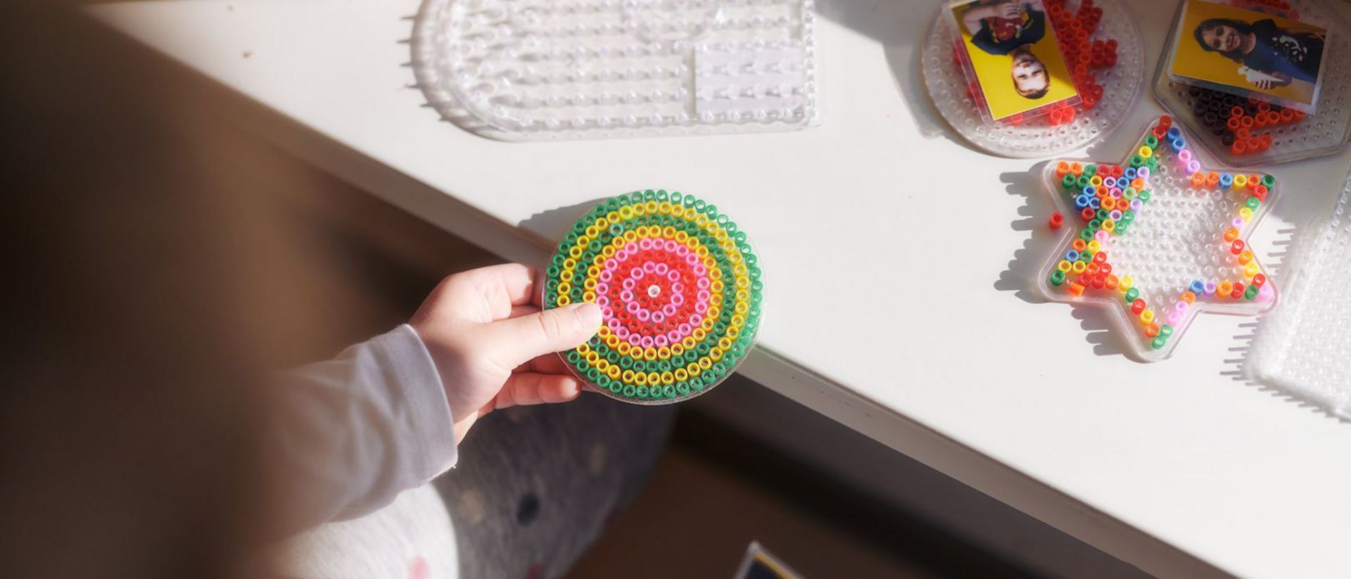 Kinderhände bereiten ein Bild aus Bügelperlen vor.