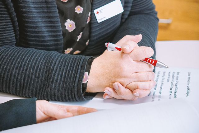Man sieht Hände, Kugelschreiber und Papiere, die an ein Beratungsgespräch erinnern.