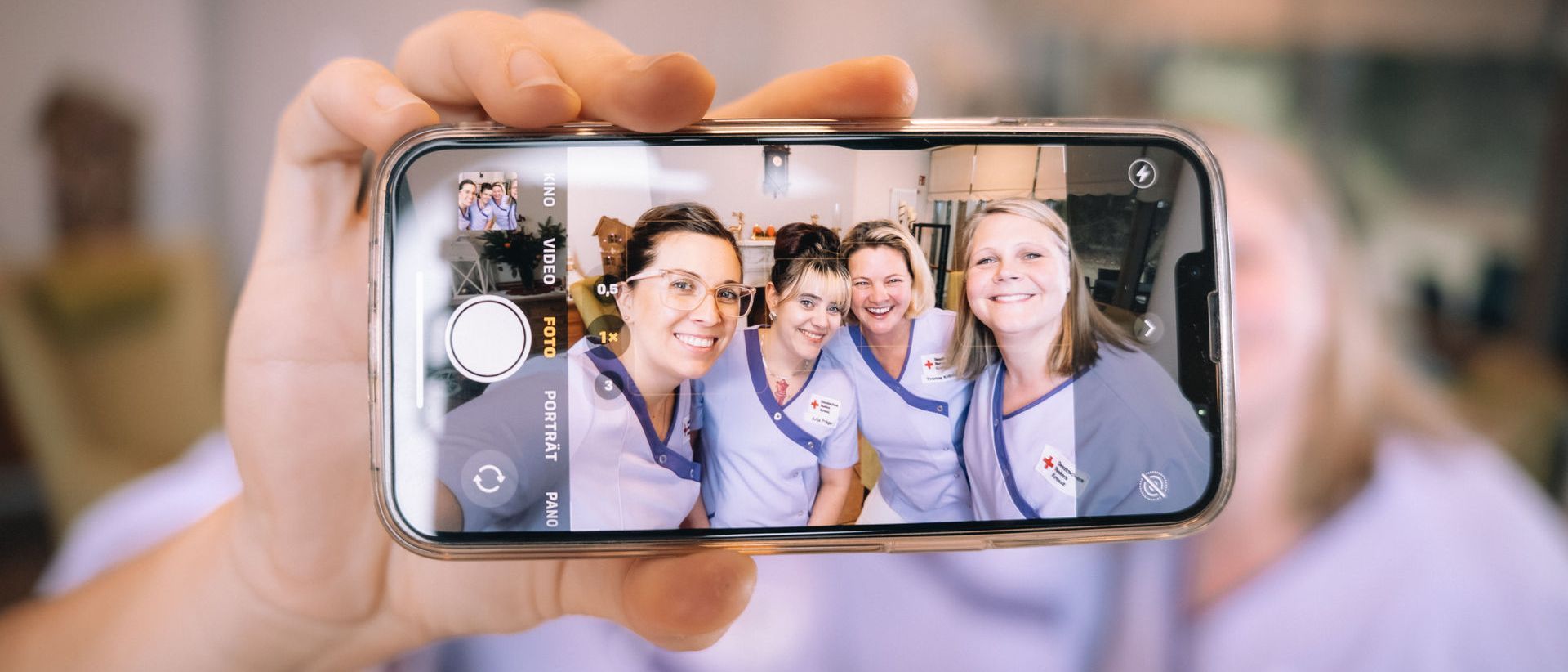 Man sieht lächelnde Mitarbeitende in Arbeitskleidung auf einem Handy-Display.