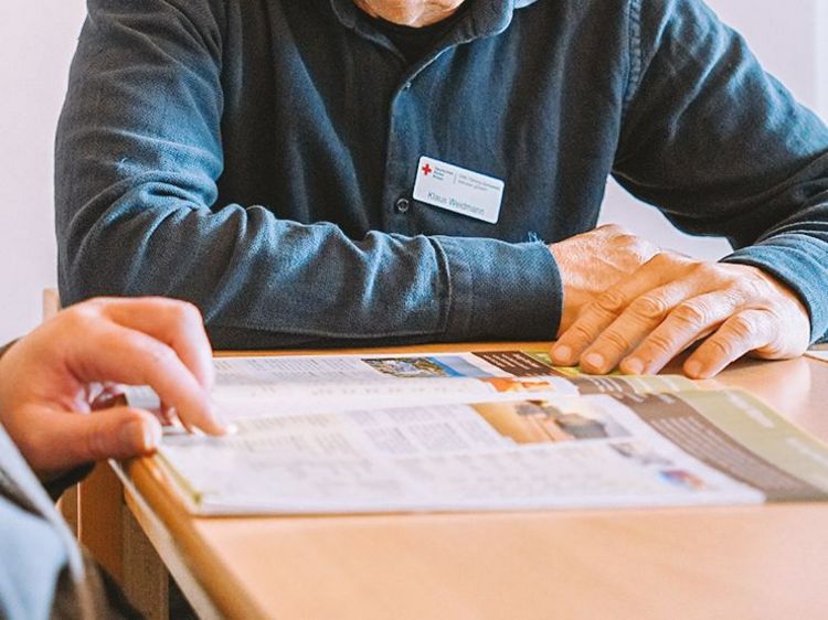 Man sieht eine aufgeschlagene Zeitung und zwei Menschen, die diese betrachten.