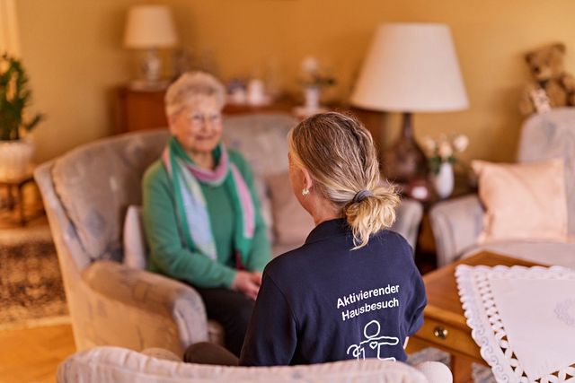DRK Mitarbeiterin und Seniorin sitzen im Wohnzimmer bei nettem Gespräch.