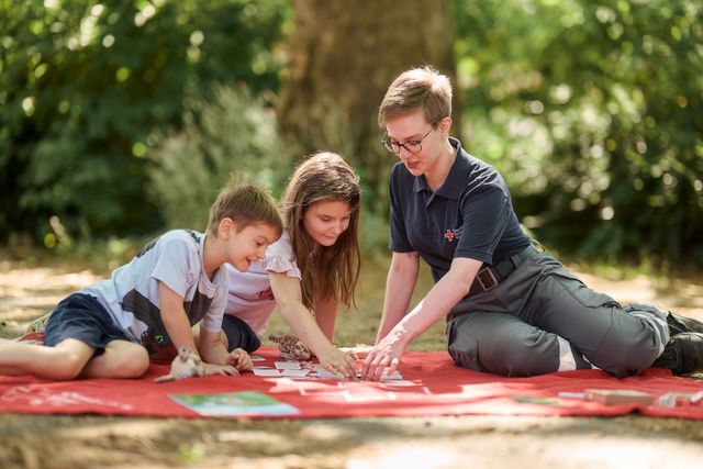Kinder und DRK-Mitarbeiterin spielen im Garten ein Kartenspiel.