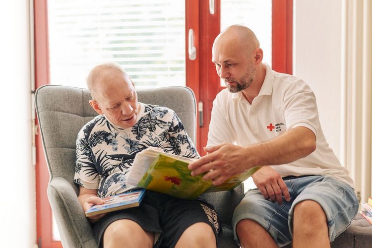 Ein Nutzer schaut sich gemeinsam mit einem Mitarbeiter unserer Besonderen Wohnform ein Buch an.