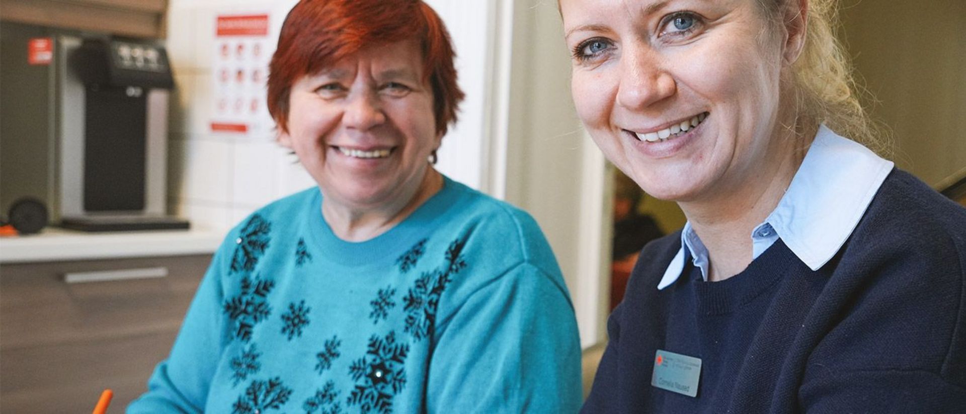 Fachkraft Inklusion und Person mit assistenzbedarf lächeln in die Kamera.