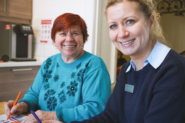 Fachkraft Inklusion und Person mit assistenzbedarf lächeln in die Kamera.