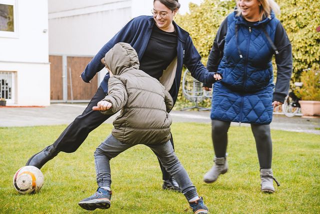 Mitarbeiterinnen spielen mit jungem Nutzer Fußball.