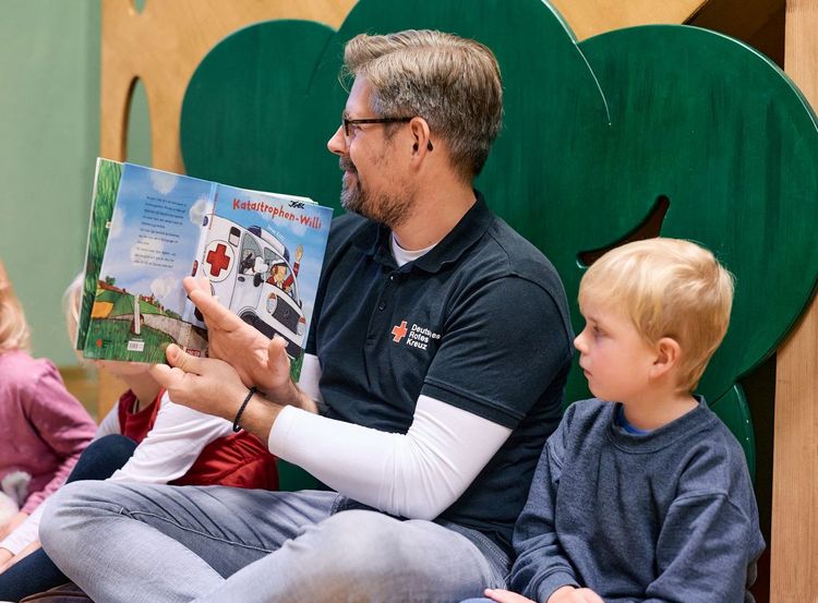 Erzieher betrachtet Buch mit Kindern.