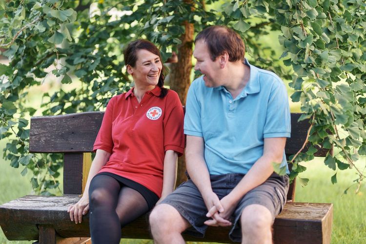 Nutzer und Mitarbeiterin der Besonderen Wohnform sitzen im Park auf der Bank.