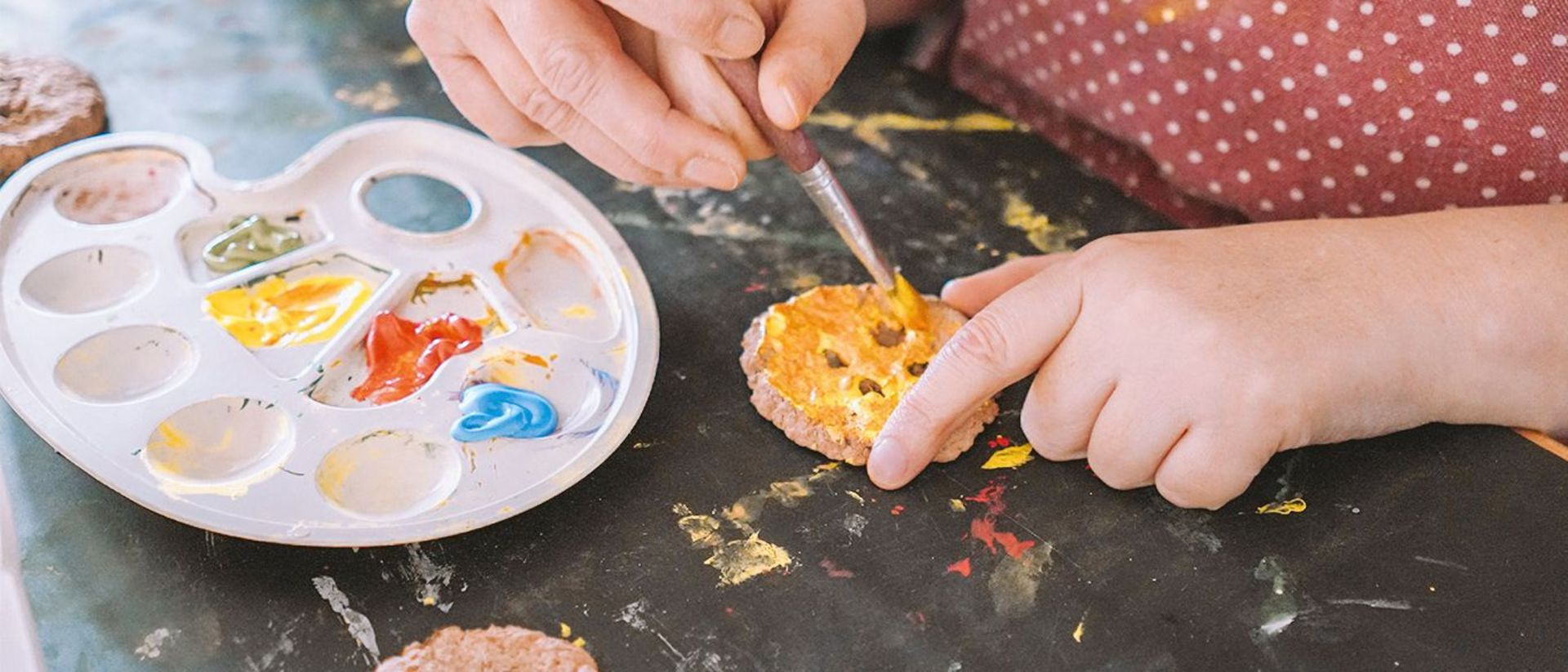 Ein Nutzender bemalt mit Unterstützung einer Fachkraft ein Werkstück.