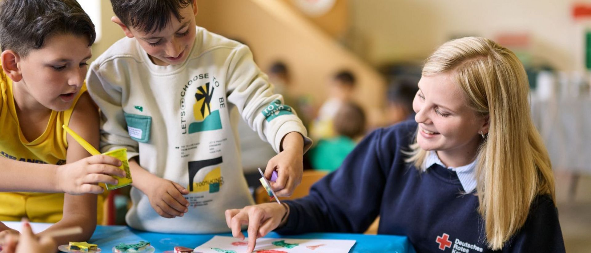 Junge Mitarbeiterin vom DRK beim Malen und Basteln mit Kindern.