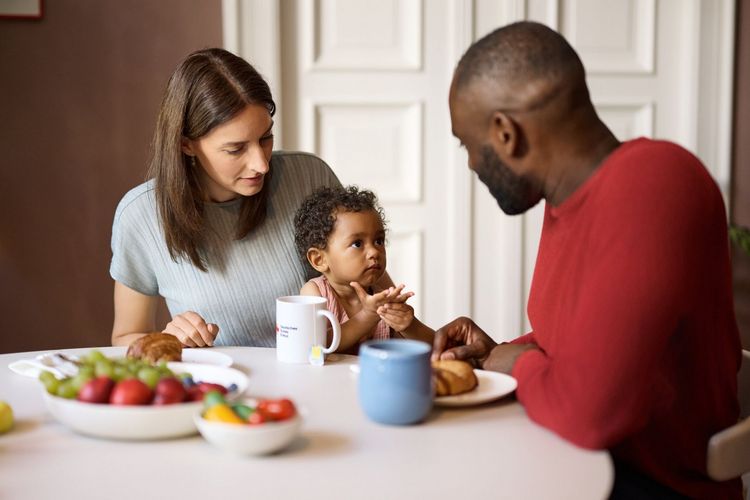 Mutter, Vater und Kleinkind am Tisch bei einer Mahlzeit.