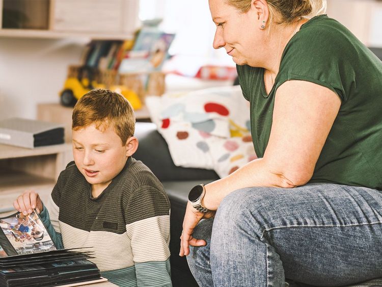 In diesem Bild sieht man einen Jungen, welcher in unserer Besonderen Wohnform Mozartkids lebt und sich gemeinsam mit einer unserer Fachkräfte ein Fotoalbum ansieht.