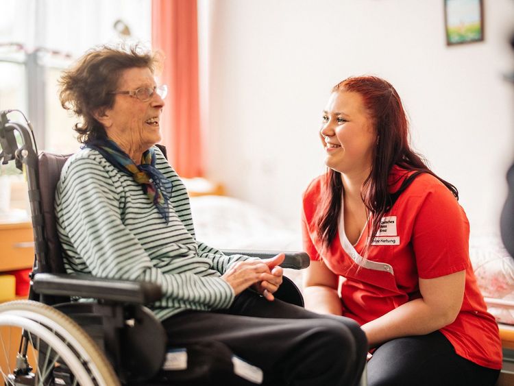 DRK Mitarbeiterin unterhält sich mit Seniorin im Rollstuhl.