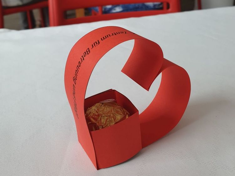 Man sieht ein gebasteltes Herz auf einem Tisch.