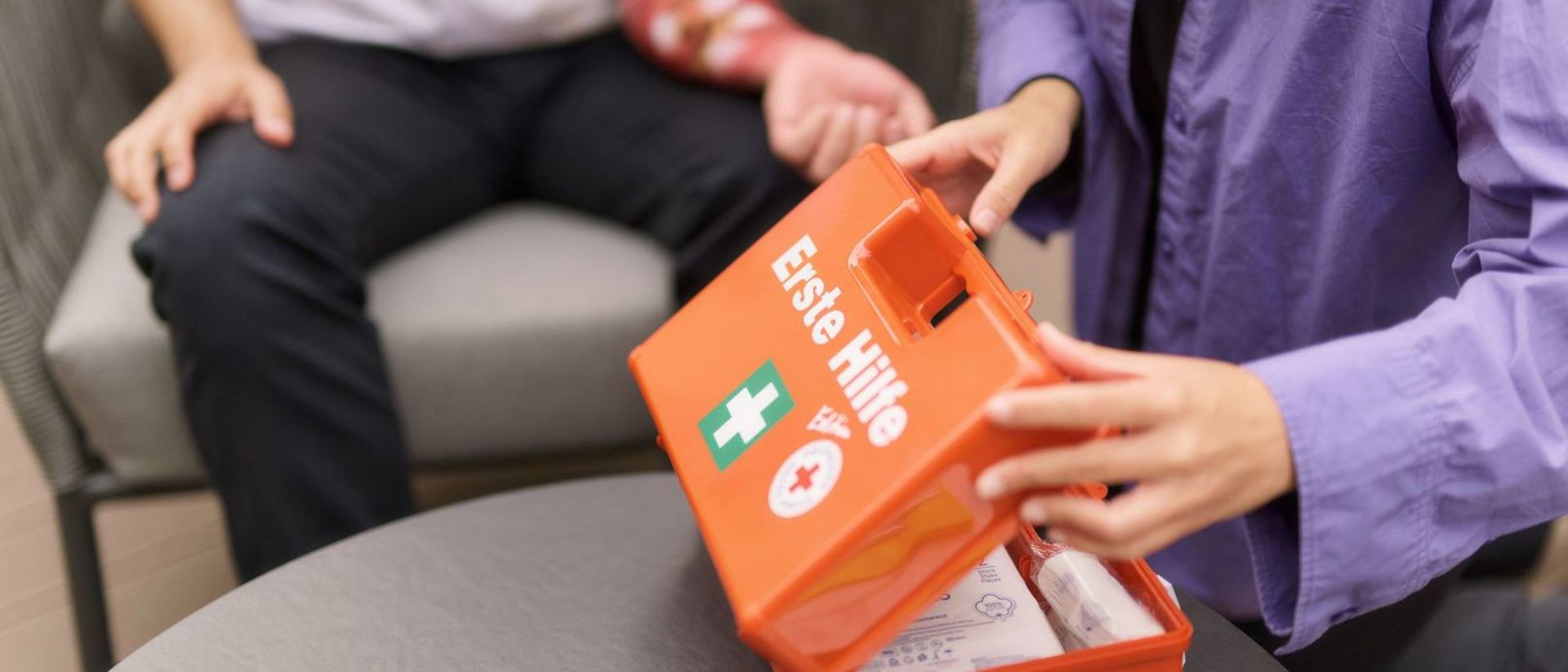 Erste-Hilfe-Koffer und verletzter Arm im Hintergrund.
