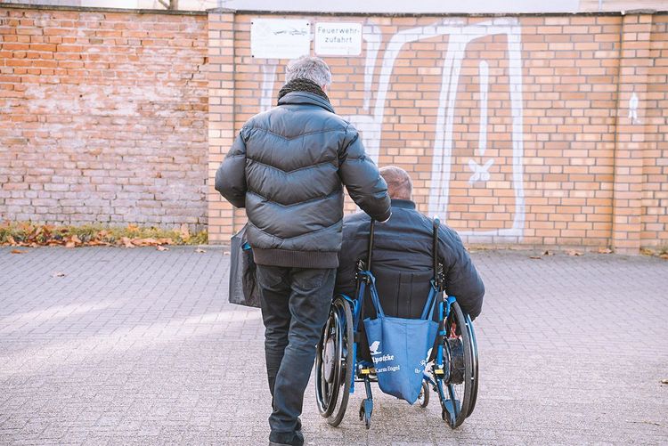 Eine Fachkraft begleitet einen Rollstuhl-Fahrer bei einem Ausflug.