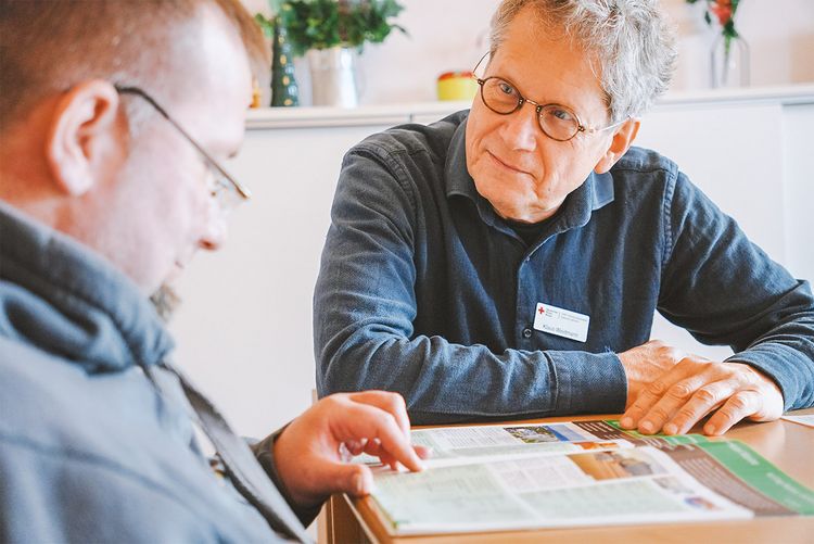 DRK Mitarbeiter und Nutzer mit Teilhabeeinschränkung sprechen gemeinsam über eine Zeitschrift.