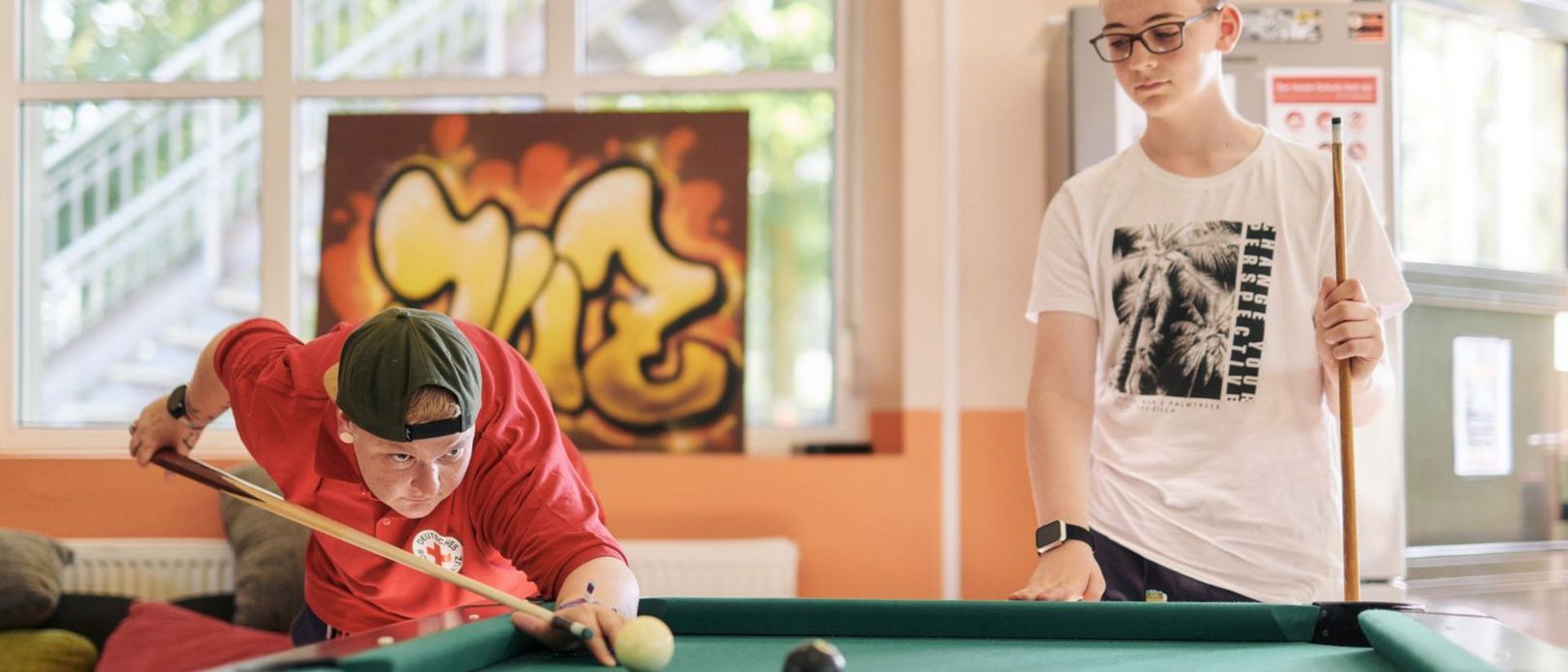 DRK Mitarbeiterin spielt Billard mit Jugendlichem.