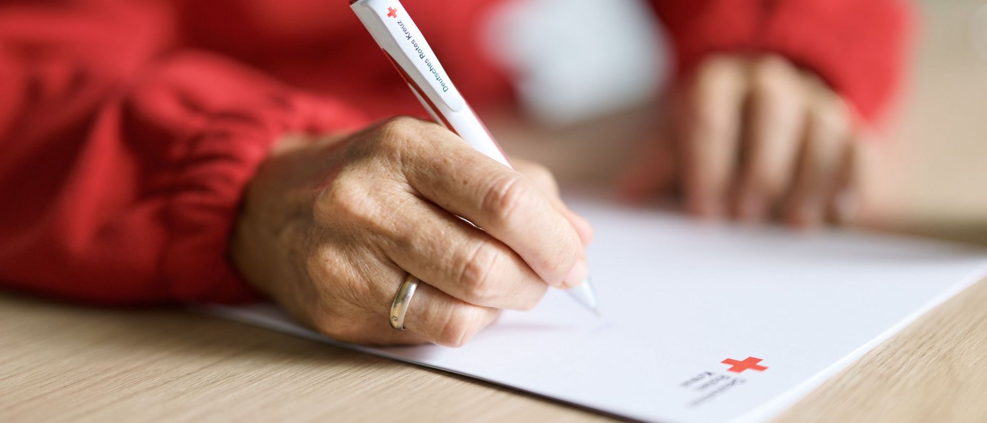 Person macht Notizen mit DRK-Kugelschreiber auf DRK-Papier.