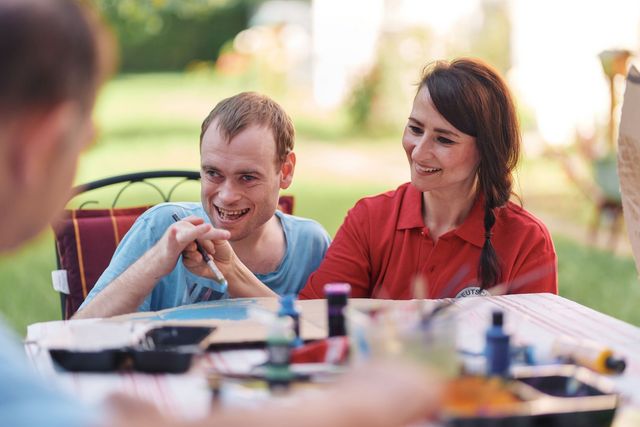 Eine Fachkraft der Besonderen Wohnform assistiert einem Nutzer beim Zeichnen.