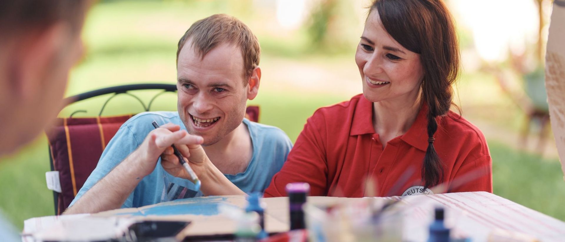 Fachkraft unserer Besonderen Wohnform assistiert Nutzer beim Zeichnen.
