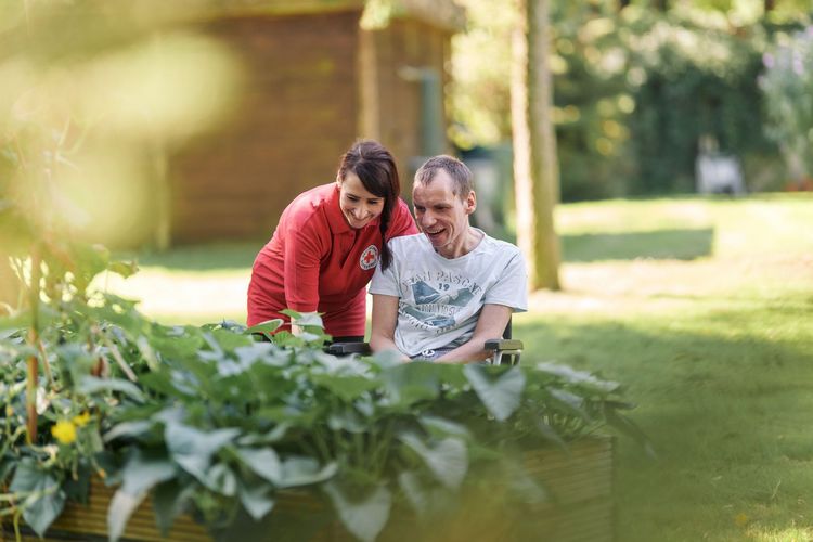 Mitarbeiterin der Besonderen Wohnform bestaunt gemeinsam mit Nutzer die Pflanzen im großzügigen Park der Einrichtung.