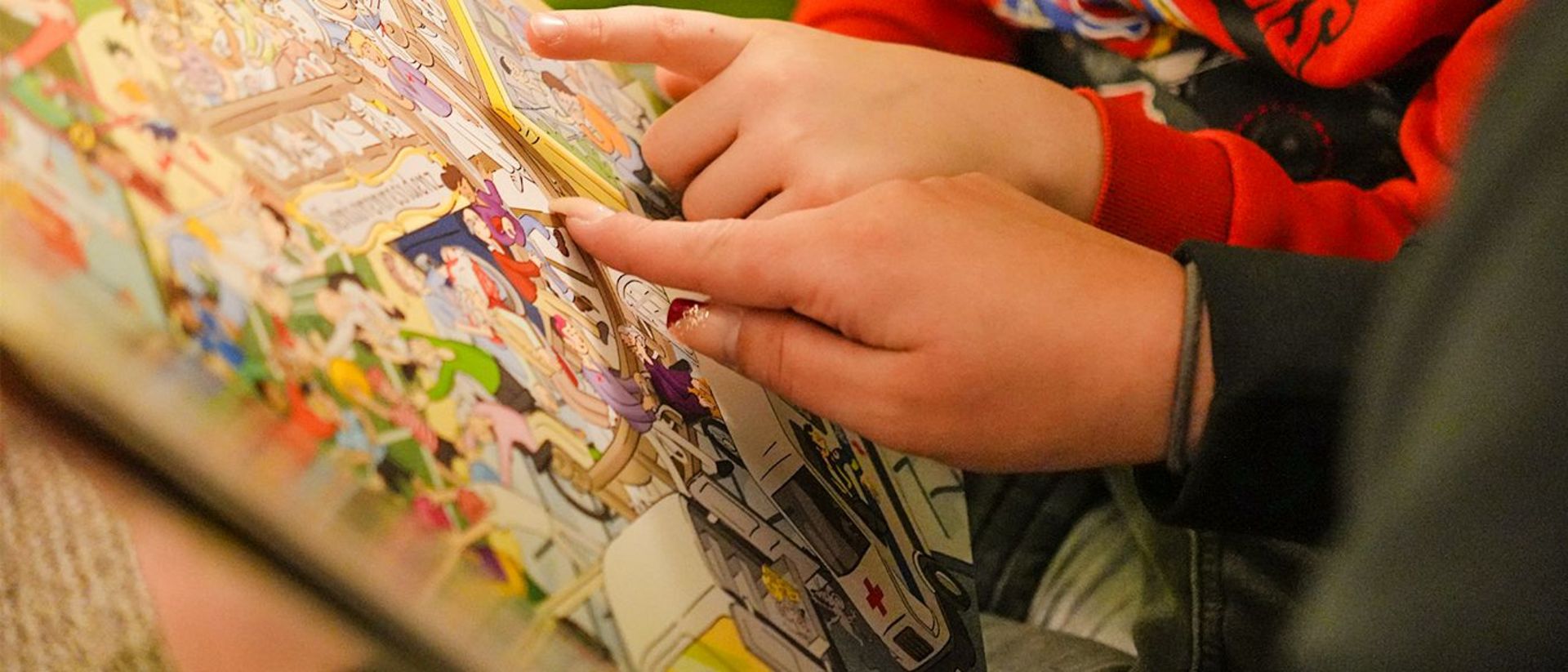 Die Hände eines Kindes und einer Mitarbeiterin des Familienentlastenden Dienstes fahren eine Buchseite nach.