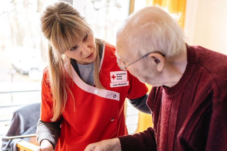 DRK Mitarbeiterin spricht mit pflegebedürftigem Senior.
