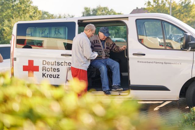 Mitarbeiter des DRK-Fahrdienst hilft Senior aus dem Kleinbus.