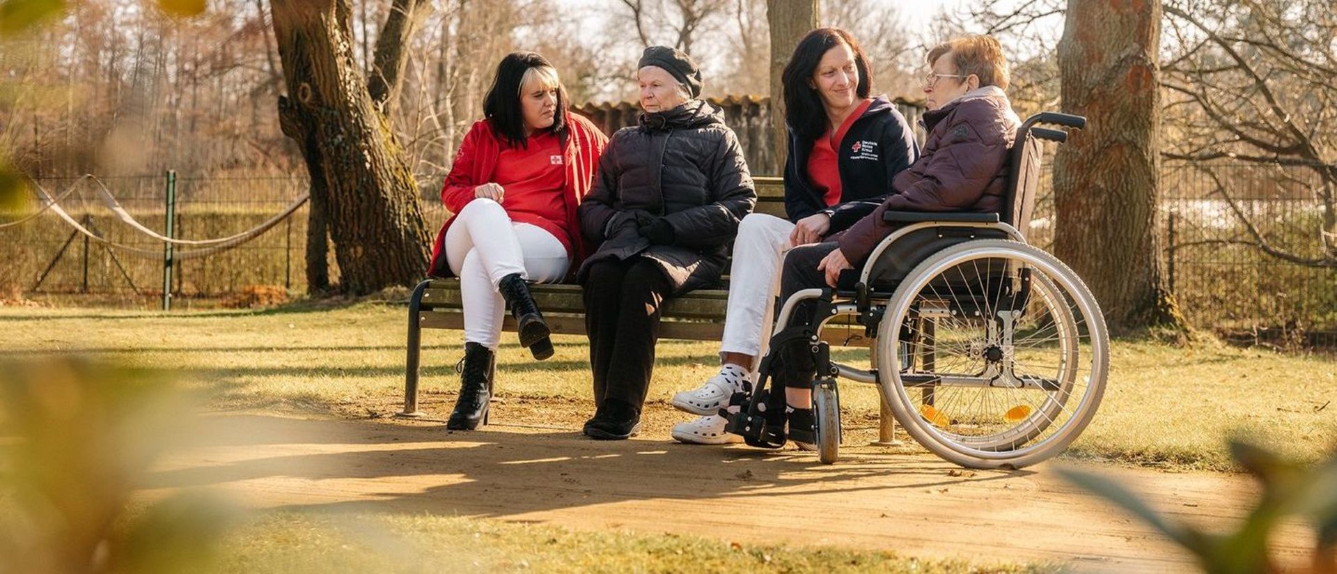 Mitarbeiter der Seniorenpflege sitzen mit Senioren auf einer Bank im Park.