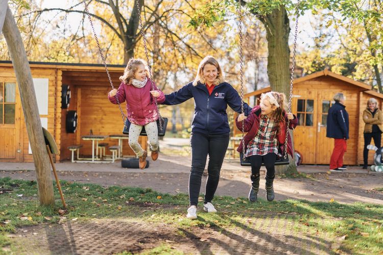 Erzieherin schubst zwei Kinder auf der Schaukel an.