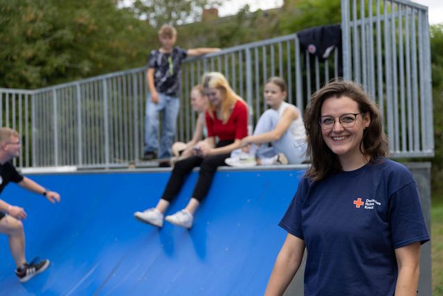 DRK Mitarbeiterin steht an Halfpipe mit Jugendlichen im Hintergrund.