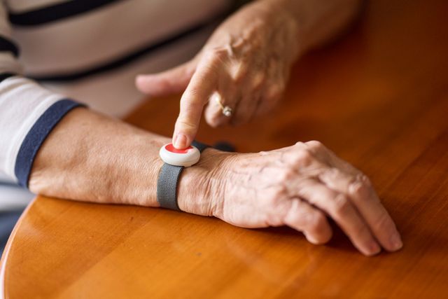 Man sieht das Armband mit dem Hausnotrufknopf am Handgelenk einer Seniorin.