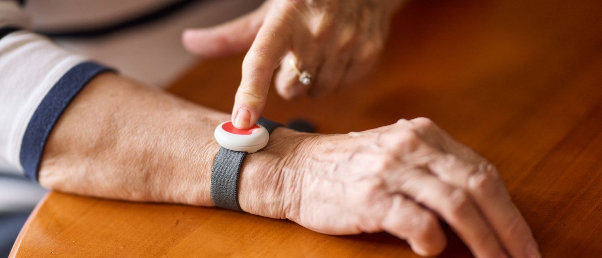 Man sieht das Armband mit dem Hausnotrufknopf am Handgelenk einer Seniorin.
