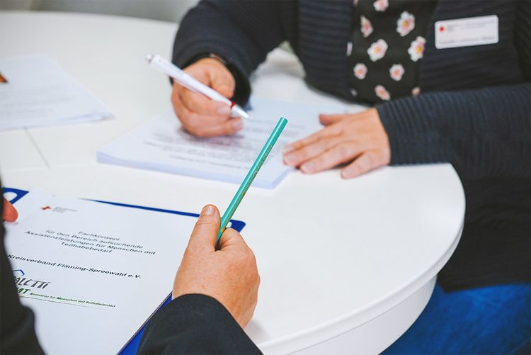 Man sieht zwei Personen an einem Tisch mit Papierkram.
