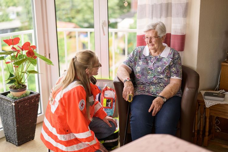 Seniorin mit Hausnotruf-Armband unterhält sich mit DRK-Mitarbeiterin.