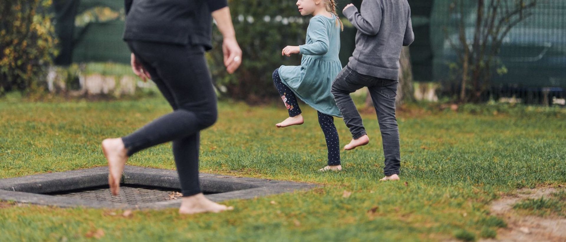 Erzieherin und Kinder laufen barfuß durch den Garten.
