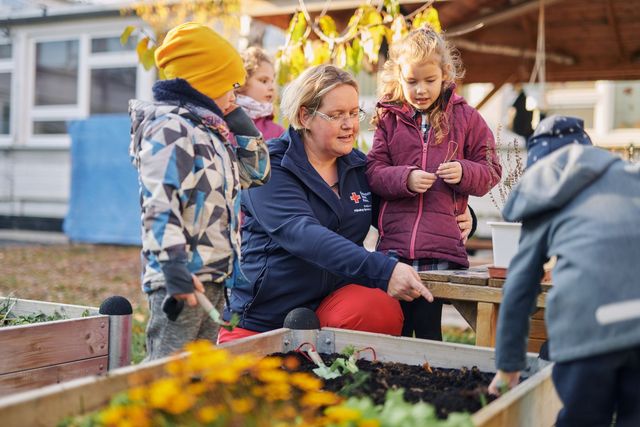Erzieherin erklärt Kindern etwas am Hochbeet.