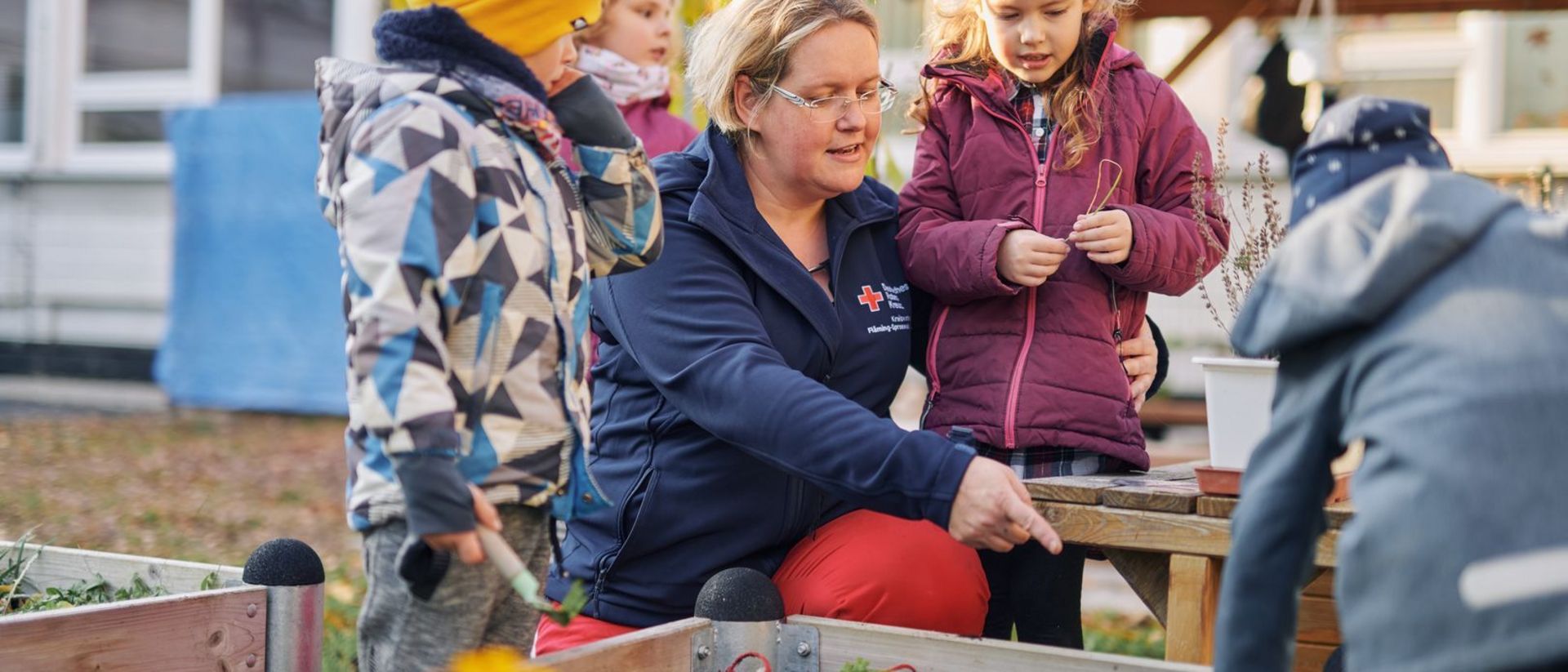 Erzieherin erklärt Kindern etwas am Hochbeet.