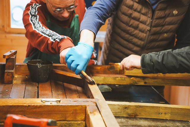 Holz wird von einem Nutzer mit Unterstützung einer weiteren Person bearbeitet.