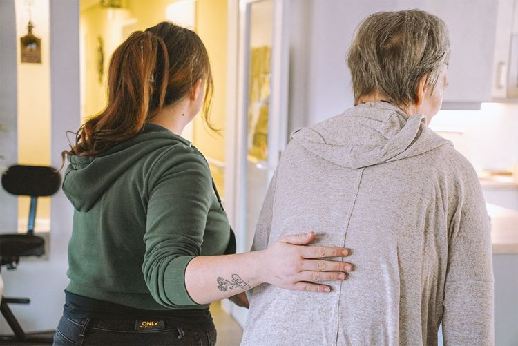 Mitarbeiterin und Nutzerin laufen nebeneinander und Mitarbeiterin legt Hand stützend auf den Rücken.