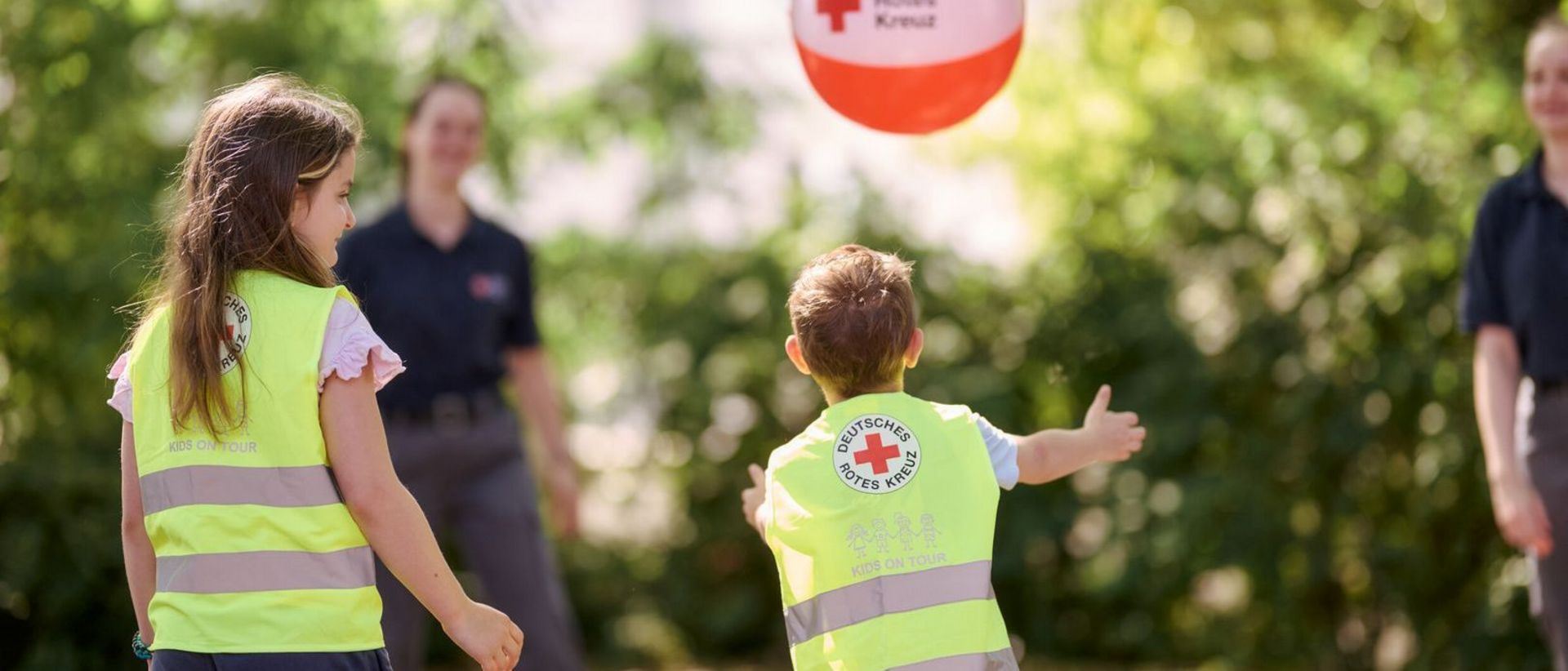Kinder und DRK-Mitarbeiter spielen im Garten mit einem Ball.