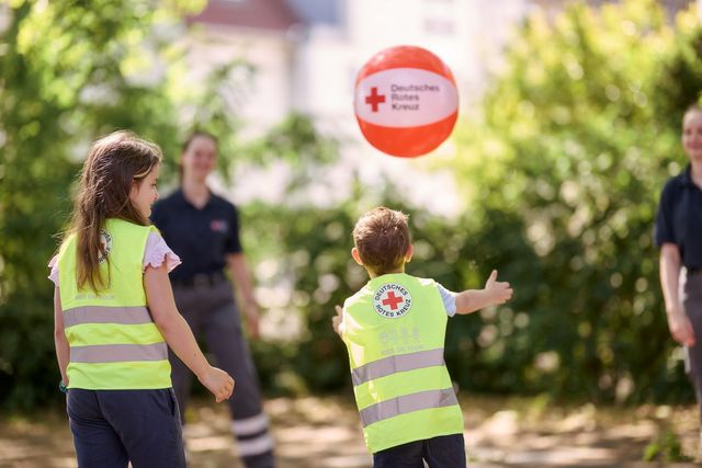 Kinder und DRK-Mitarbeiter spielen im Garten mit einem Ball.