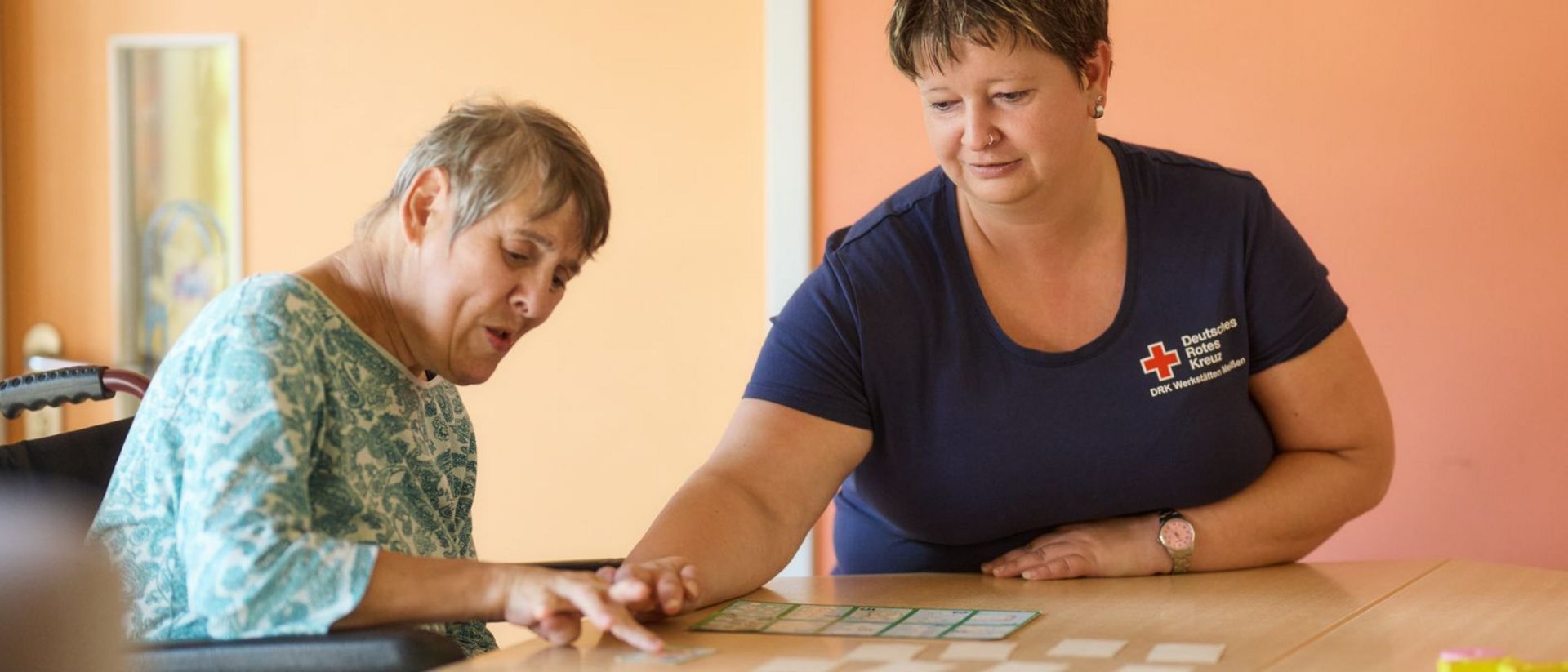 DRK Mitarbeiterin spielt mit Dame mit Teilhabeeinschränkung ein Spiel.